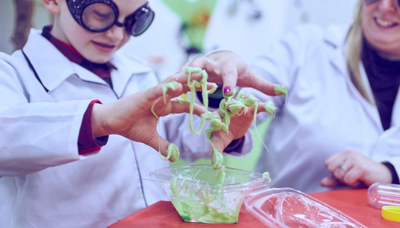 A child wearing a lab coat and goggles and playing with slime