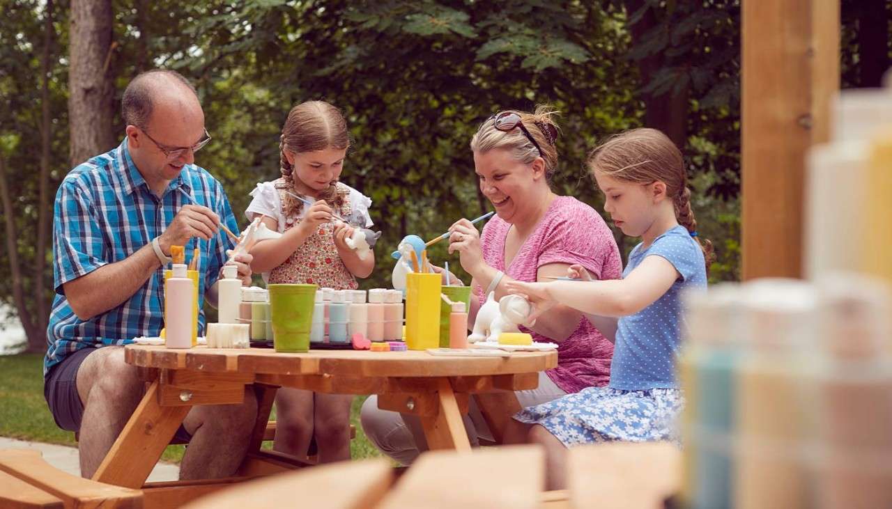 A family sat on an outdoor picnic table painting pottery 