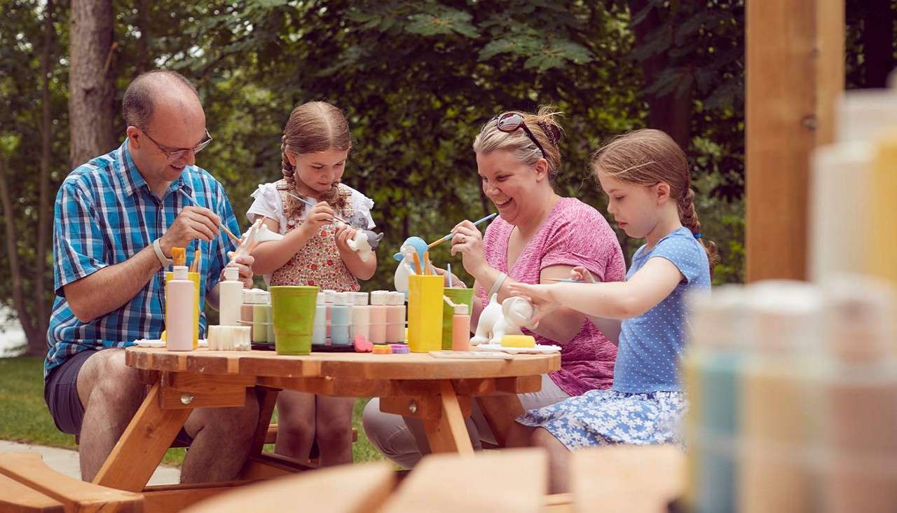 A family sat on an outdoor picnic table painting pottery 