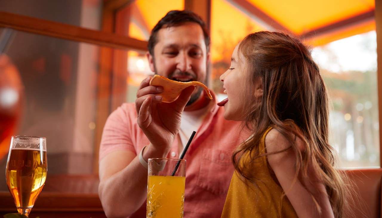 A father feeding his daughter a slice of pizza