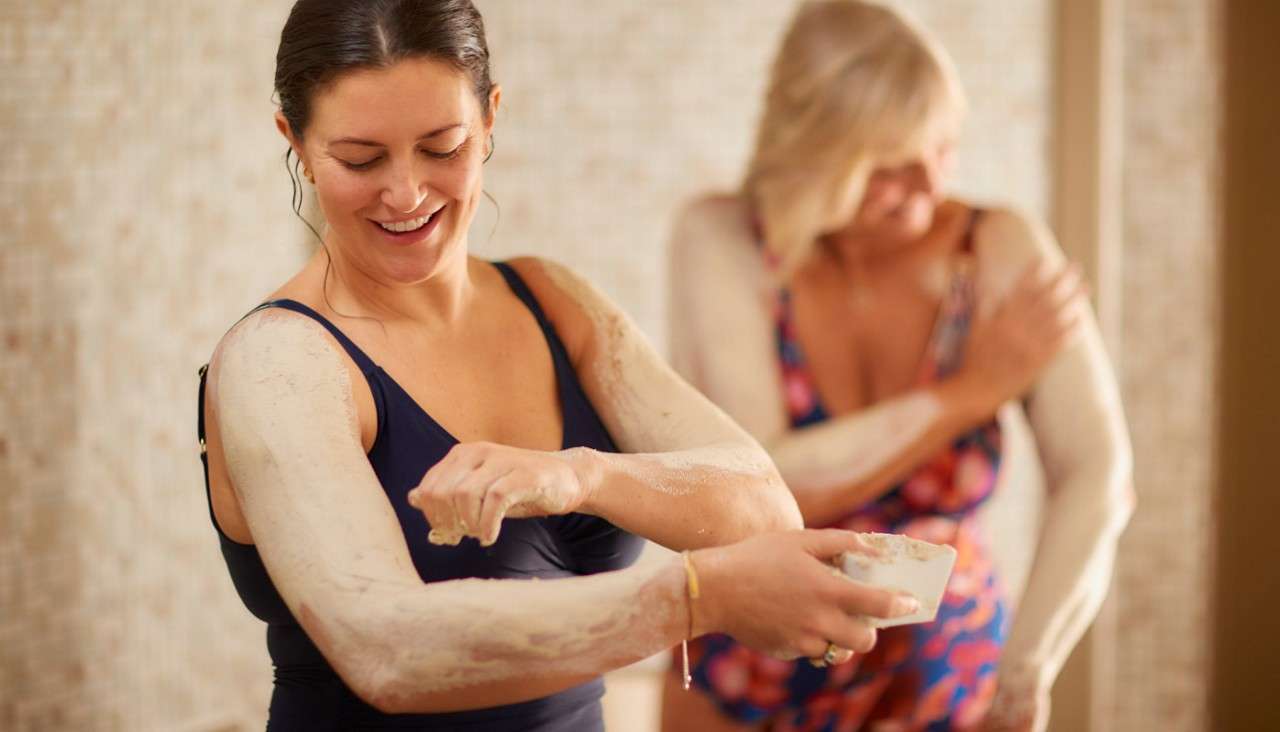Two ladies applying Serial Mud to their arms.