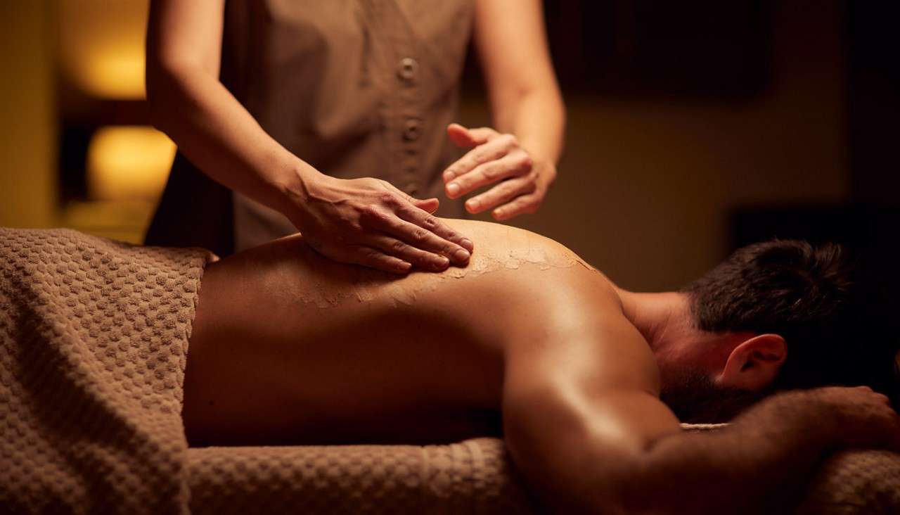 Therapist massaging a mans back with a creamy product.