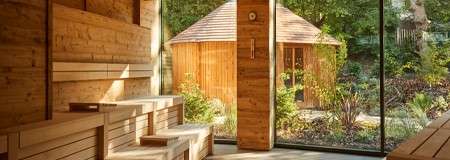 Inside a wooden sauna with a view out to the forest garden where a Scandinavian Snug sits.