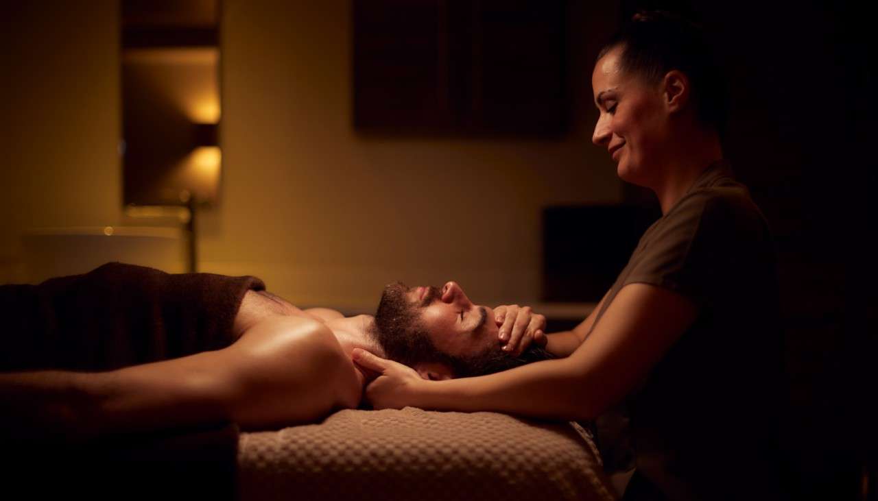 Man laying on a massage table whilst a women holds his head and neck.