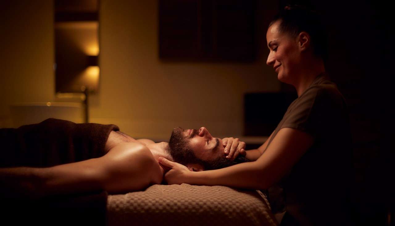 Man laying on a massage table whilst a women holds his head and neck.