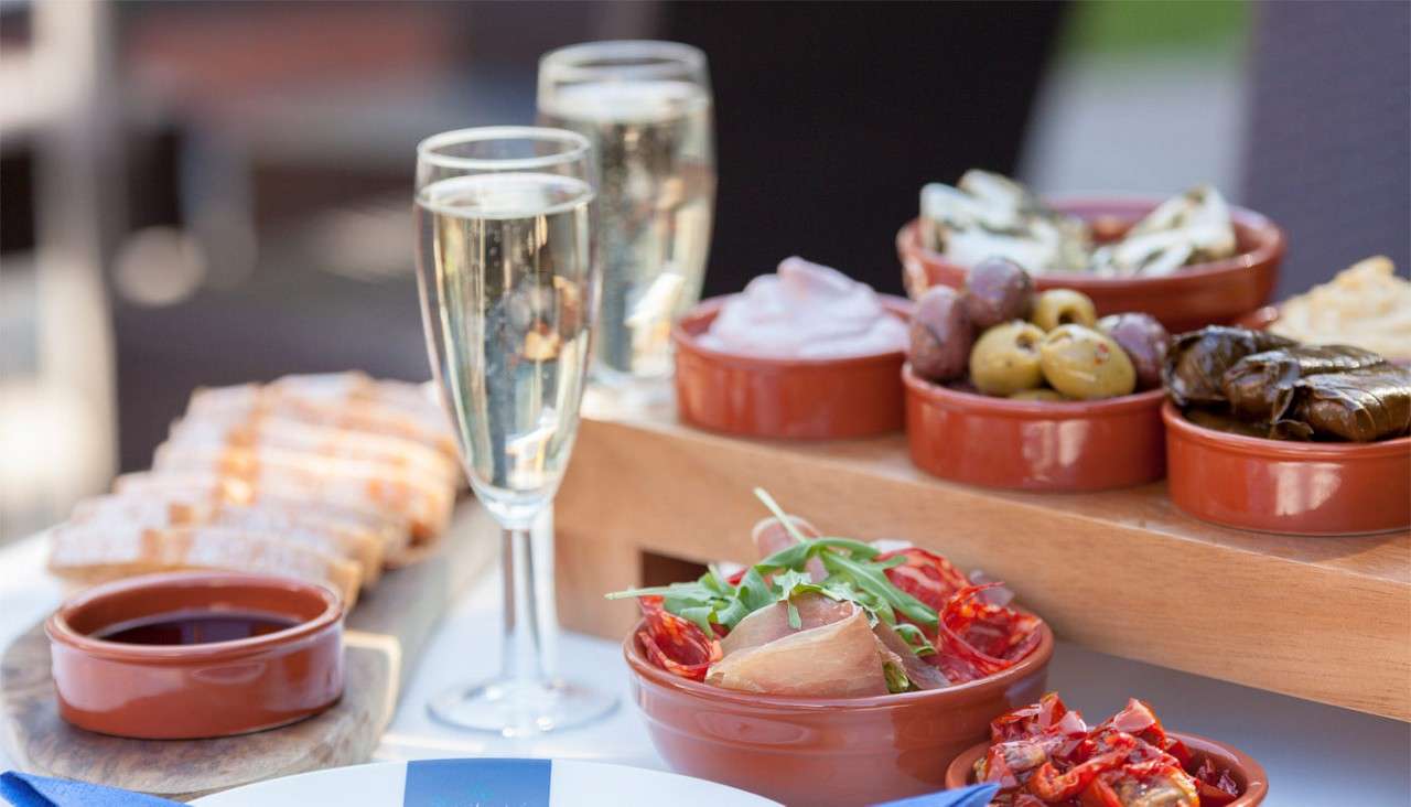 Selection of Antipasti dishes including, olives, stuffed vine leaves and houmous. Served alongside Champagne flutes.