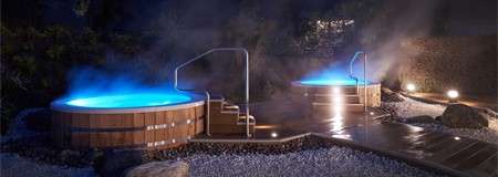 Two steaming outdoor hot tubs at night, both with steps leading up.