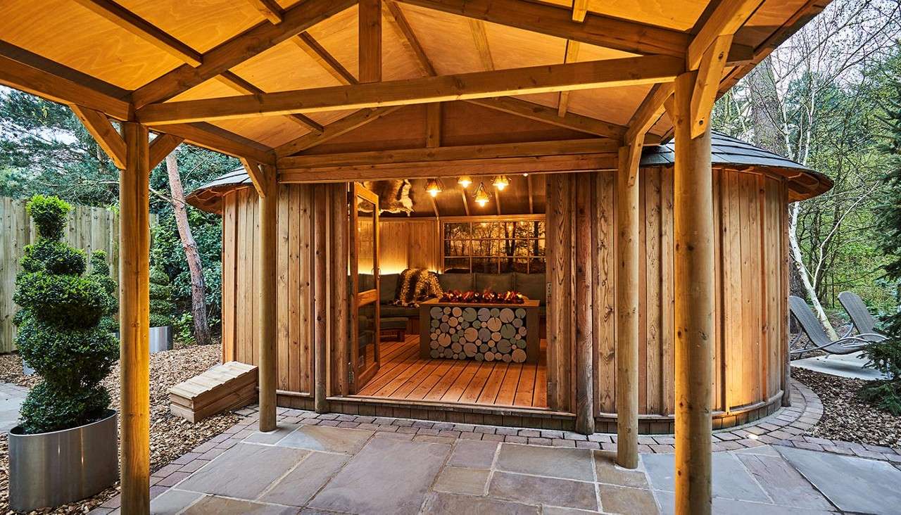 Scandinavian Snug, curved room with padded seating, pillows and blankets. A flickering fire pit and decorative animal style pelts on the roof.