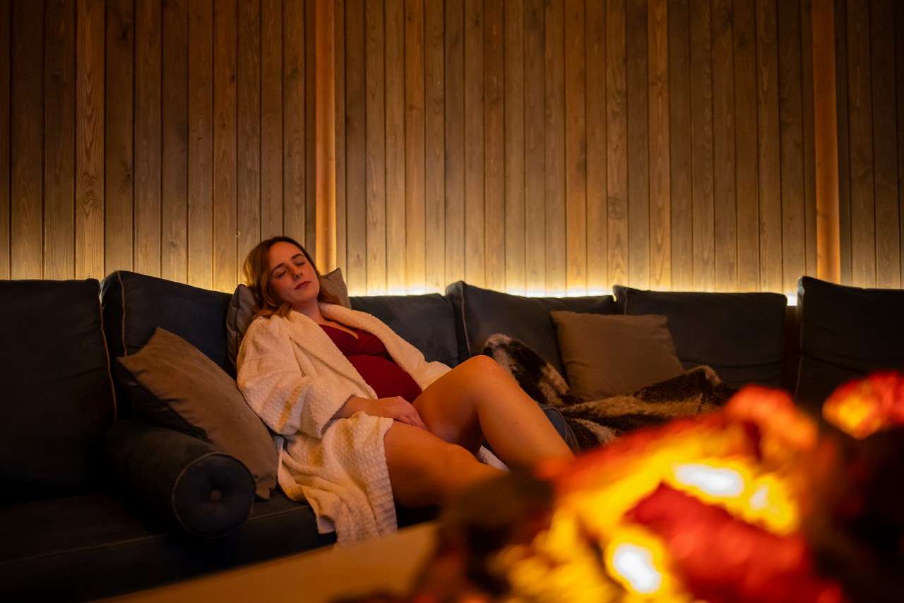 Scandinavian Snug, curved room with padded seating, pillows and blankets. A flickering fire pit and decorative animal style pelts on the roof.