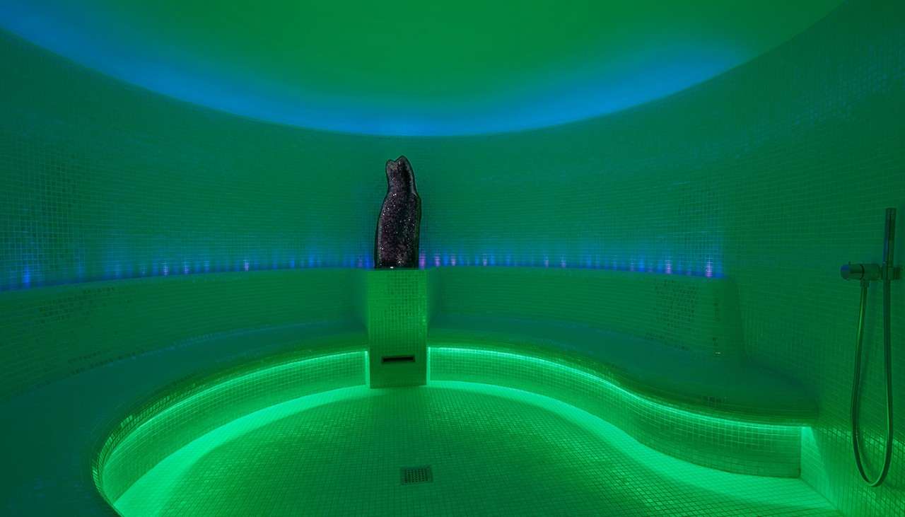 Alpine Steam room, tiled curved room illuminated in green and blue with a large amethyst crystal.