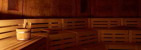 Inside of  wooden sauna with a wooden bucket on the bench.
