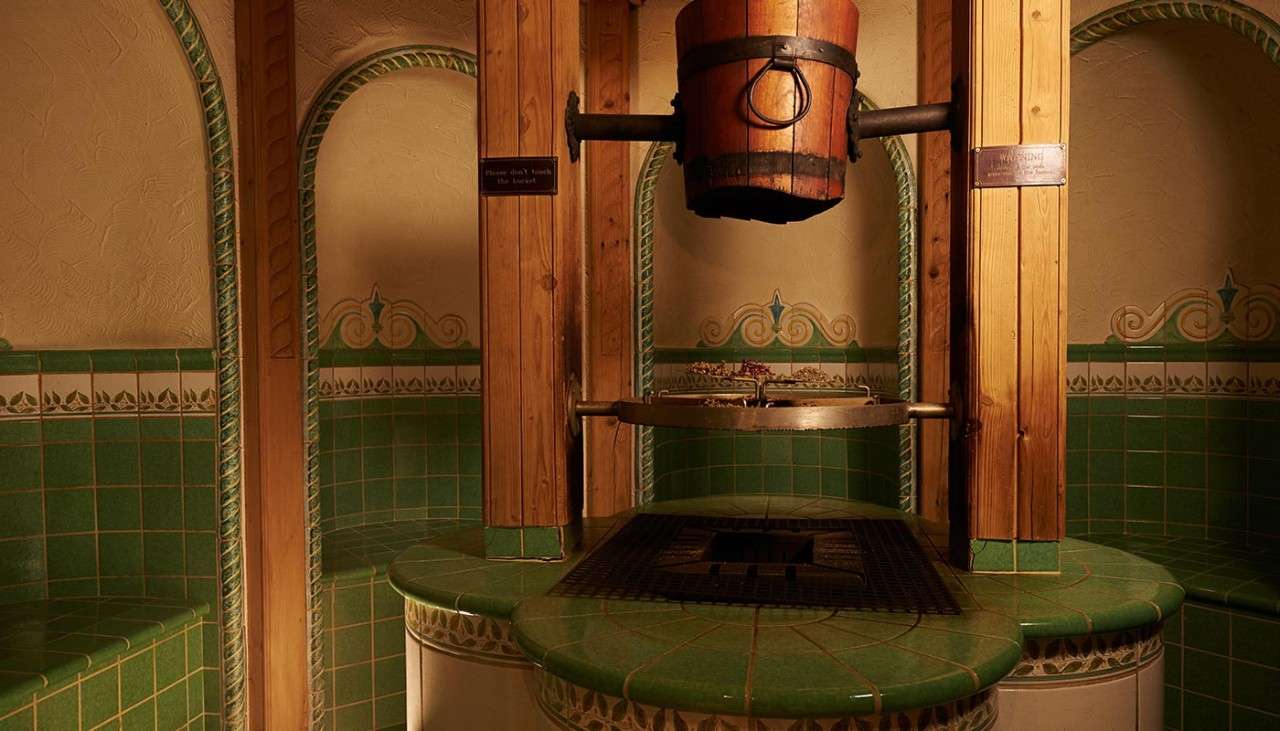 Green tiled Greek herbal bath with wooden bucket central raised above a grate.