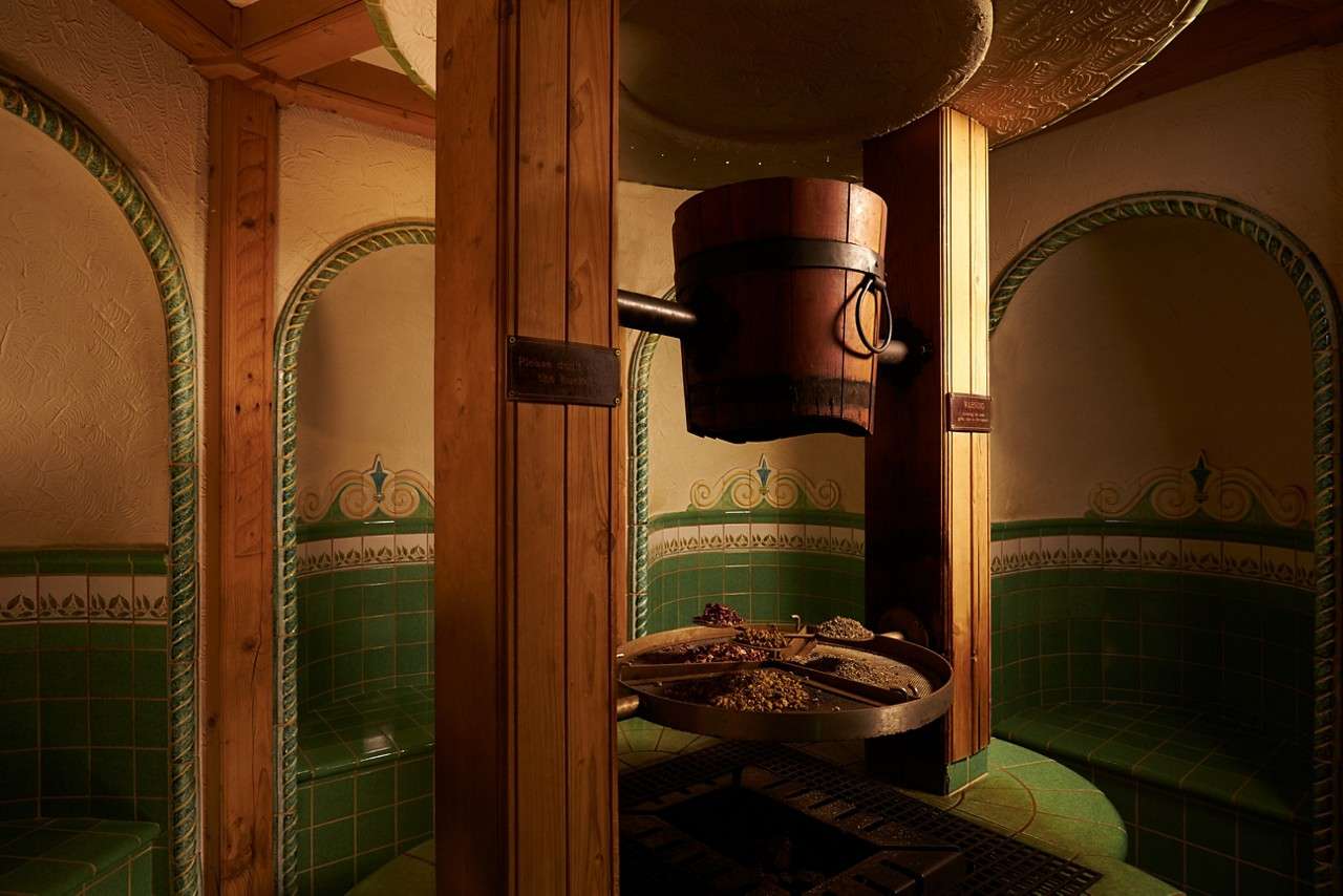 Green tiled Greek herbal bath with wooden bucket central raised above a grate.