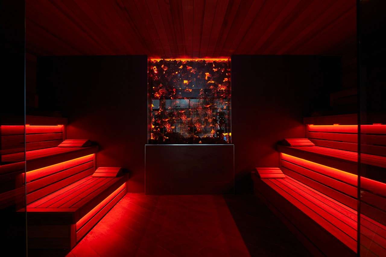 Lava Sauna with a burning coal feature wall and glowing wooden benches.
