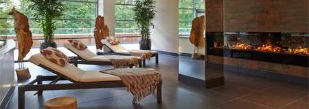 Open room with comfortable loungers, an open fire and mirrors.