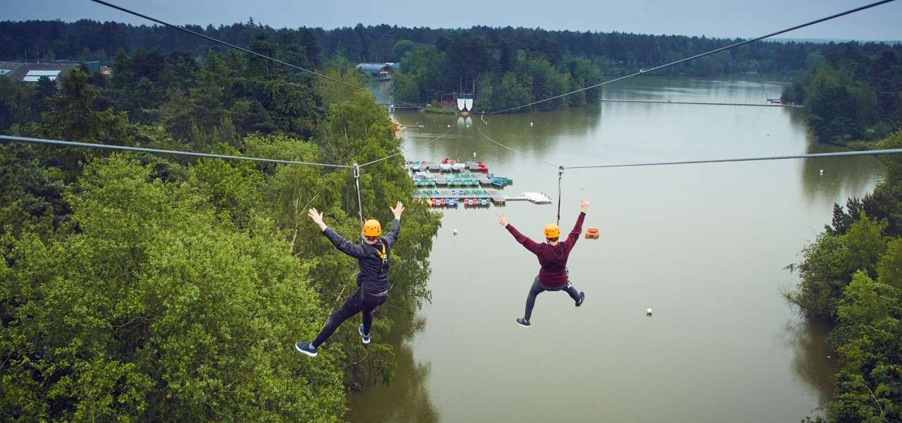 Two people going down the double zip wire over the lake 