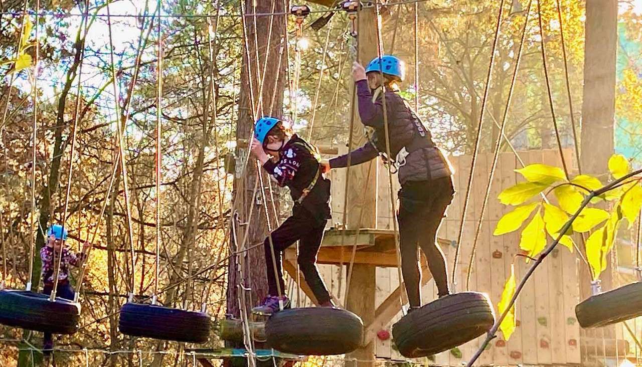 Children walking along a tyre bridge on the Aerial Adventure activity.