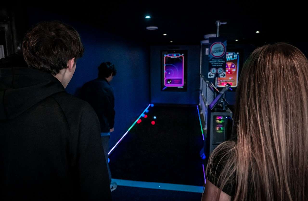 Two people playing a game of bowls in a dimly lit room with glow in the dark equipment. 