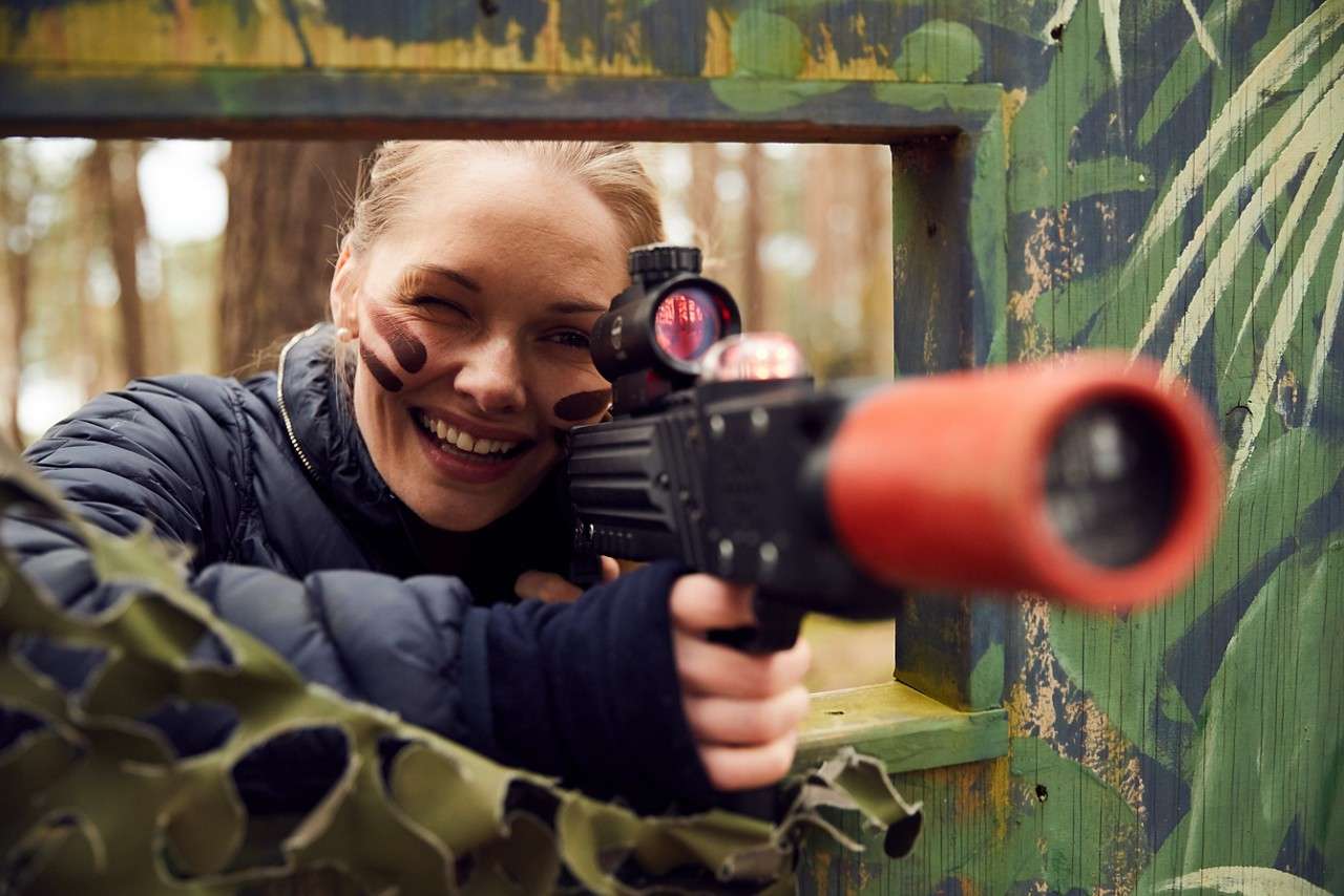 A girl peeking through a window and taking aim with a laser combat gun.
