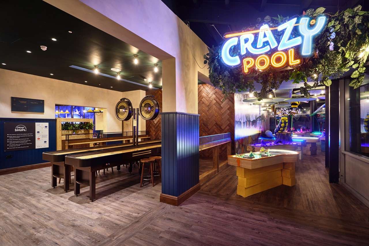 Neon sign “CRAZY POOL” glows; a gaming venue shows shuffleboard lanes with stools and decorative dials, adjoining a whimsical, illuminated mini-golf area. Visible text: “CRAZY POOL”, “How to SHUFL”.