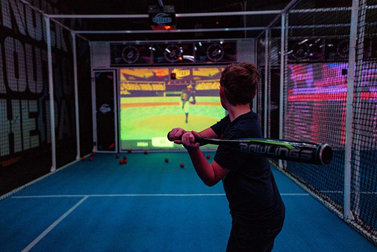 Young person playing baseball inside The Bat Cage.