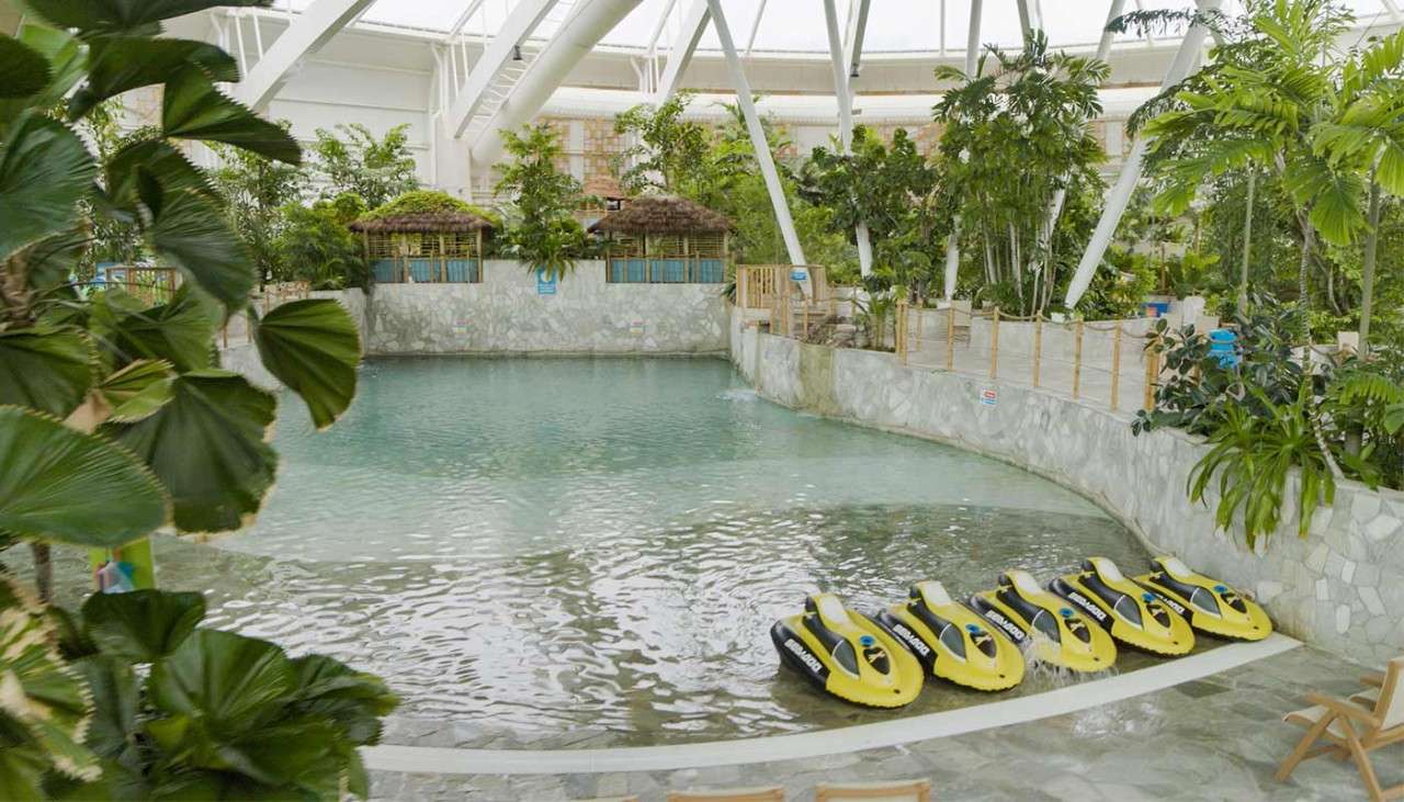 An inside image of The Subtropical Swimming Paradise pool with inflatable jet skis at the shoreline.
