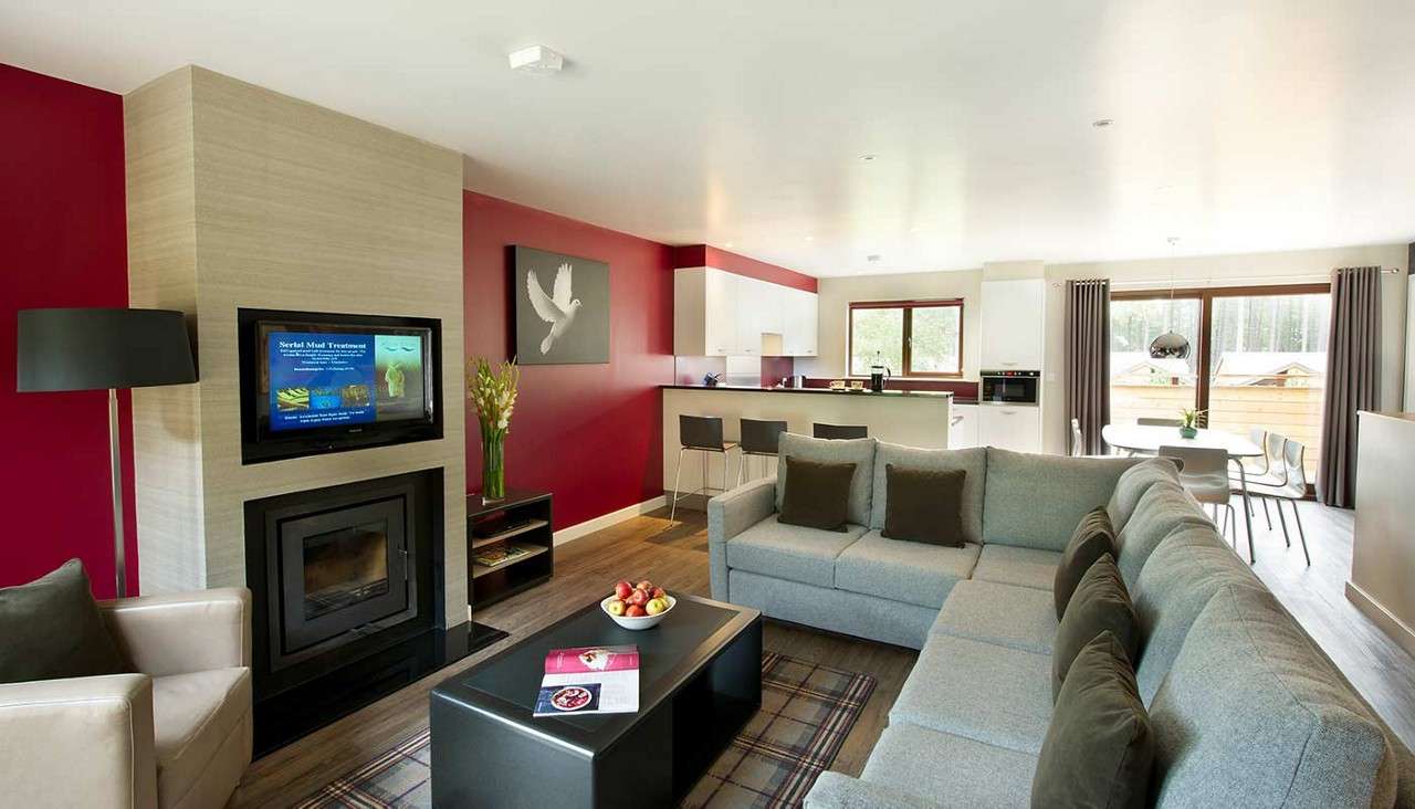 The living and dining area of an Executive Lodge. In view is a large corner sofa and fire.