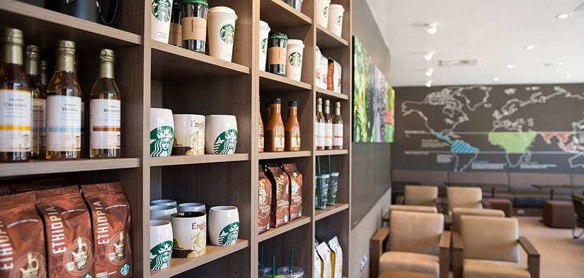 Retail shelves display Starbucks mugs, syrups, bottled drinks, and coffee bags; seating area with armchairs and a world map mural stretches behind. Visible text: ETHIOPIA.