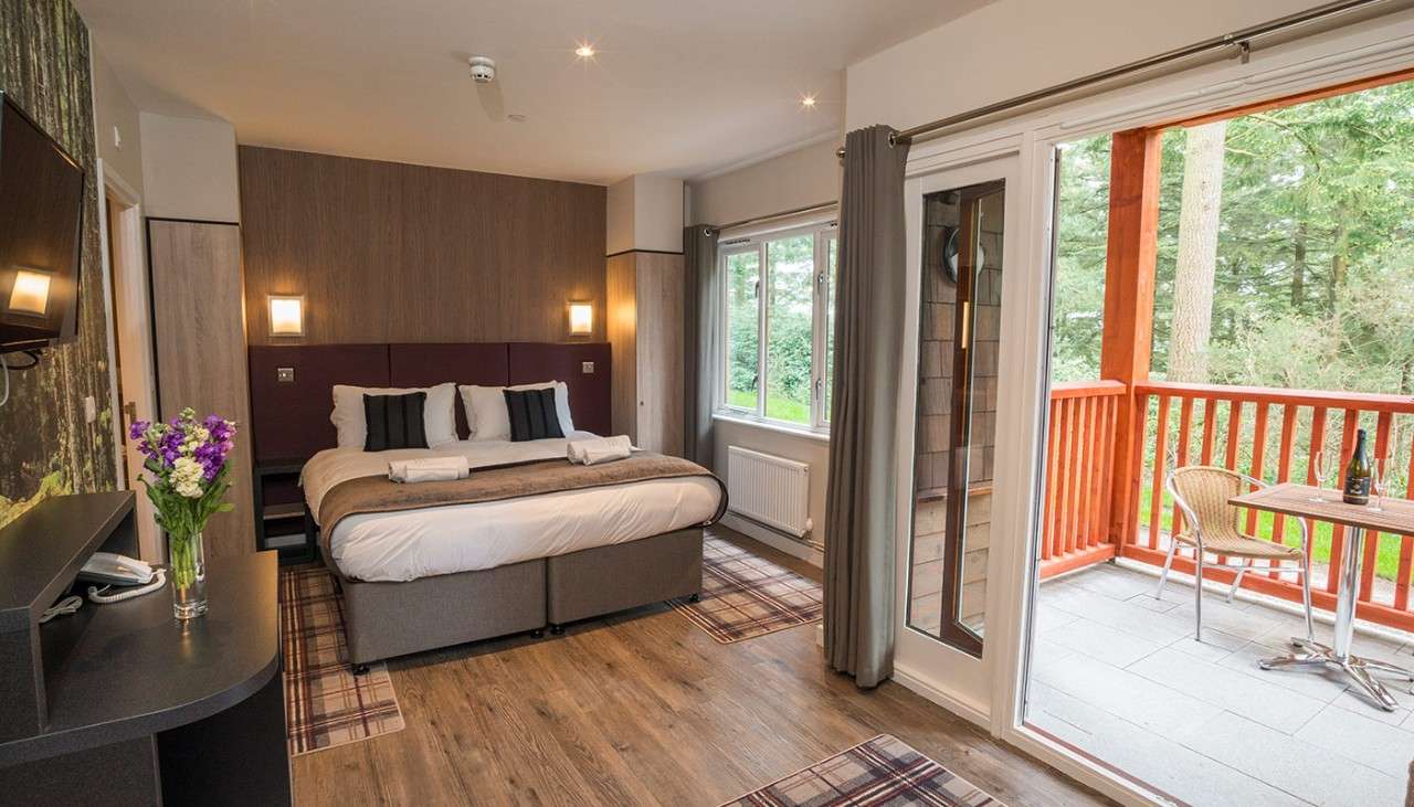 An apartment with a neatly made double bed and a balcony facing into the forest available at Longleat Forest 