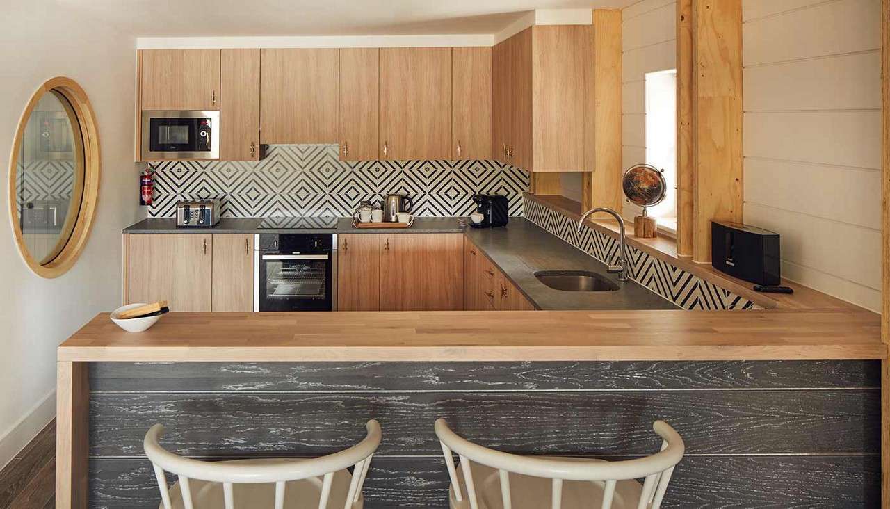 A kitchen in a Waterside Lodge with a hob, oven, sink and a bar style counter with high chairs