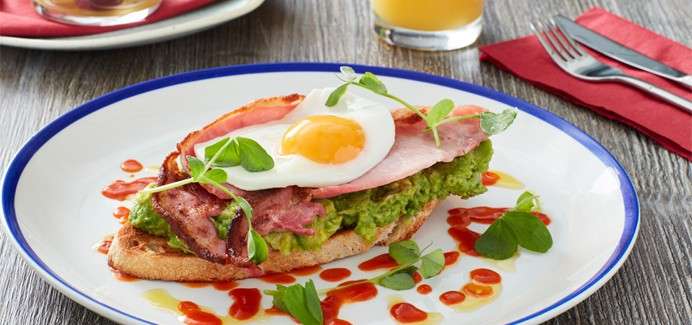  Avocado on toast topped with bacon and a fried egg.