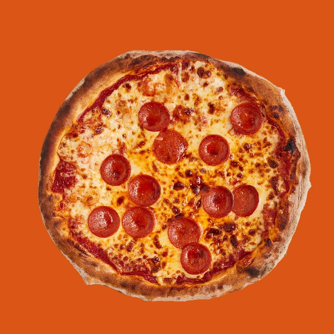Whole pepperoni pizza resting, topped with melted cheese and pepperoni slices, on a plain orange backdrop.