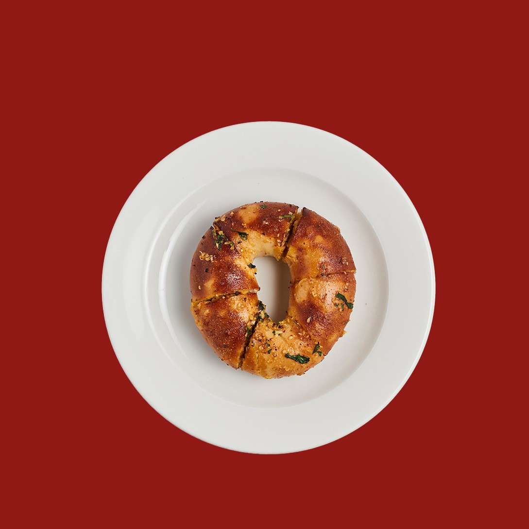 A sliced ring-shaped bread rests on a white plate, sprinkled with herbs and crumbs, set against a solid red background.