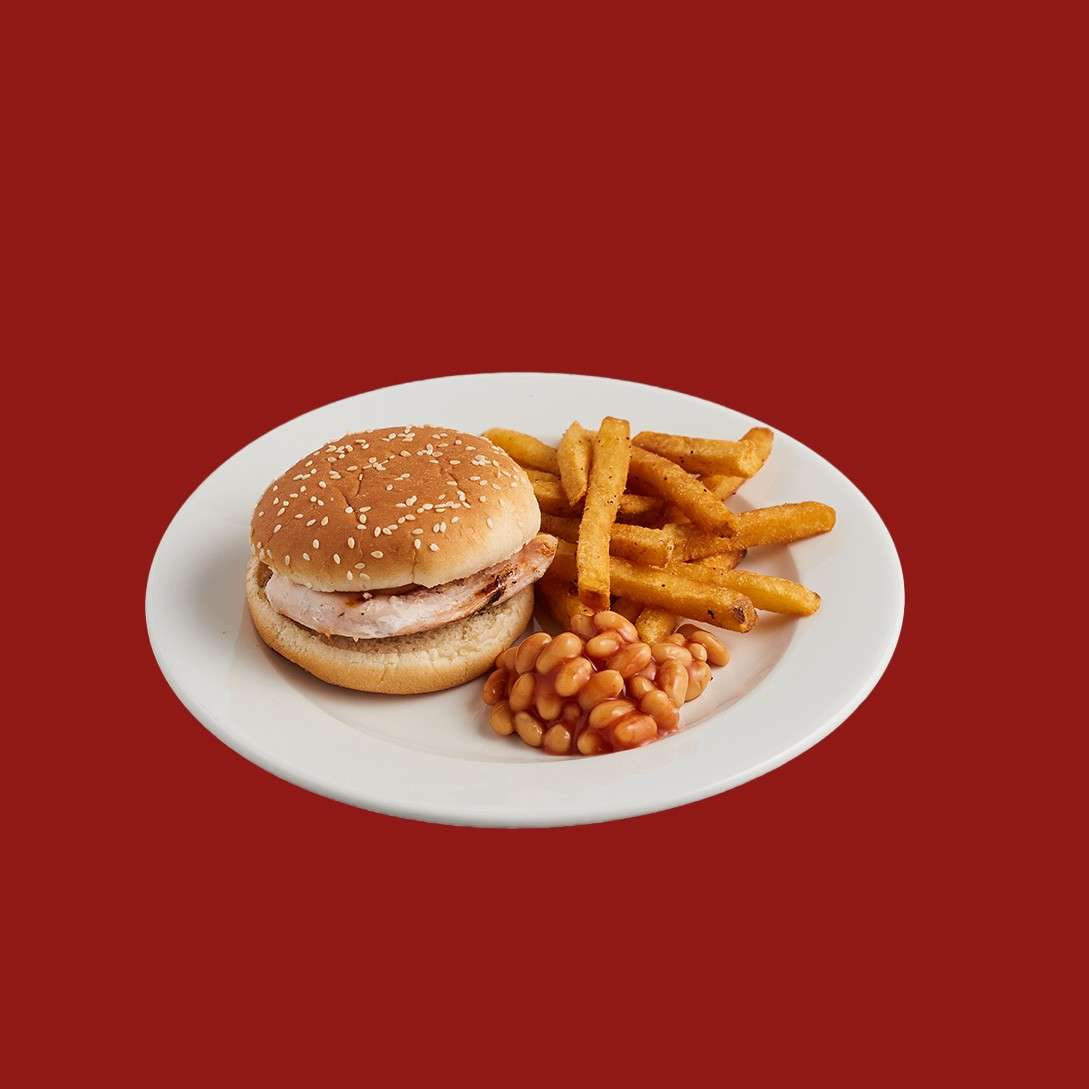 Burger sits on a white plate, accompanied by seasoned fries and baked beans, presented against a solid red background, suggesting a simple diner-style meal.