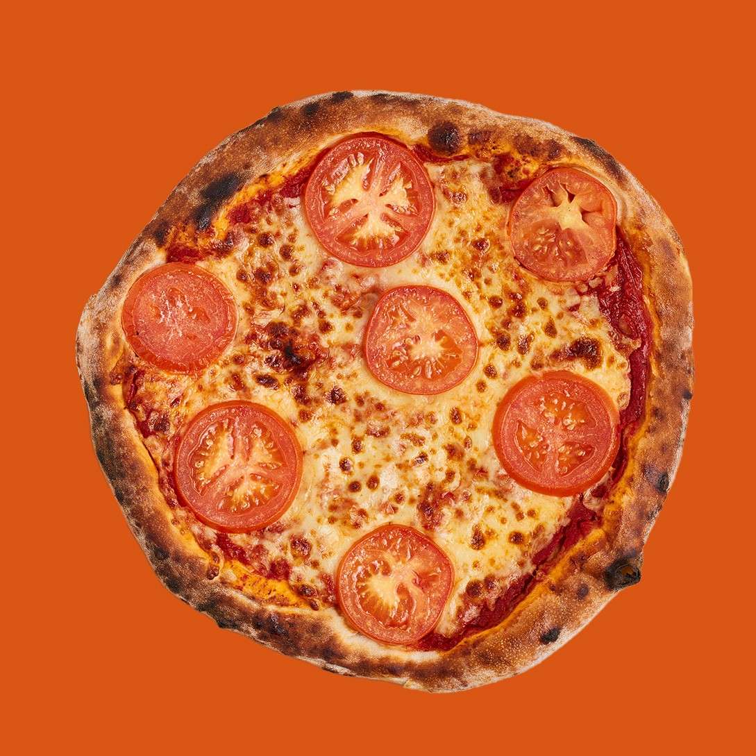 A tomato-topped cheese pizza sits flat against a solid orange background, showing browned crust, melted cheese, and six tomato slices arranged evenly.