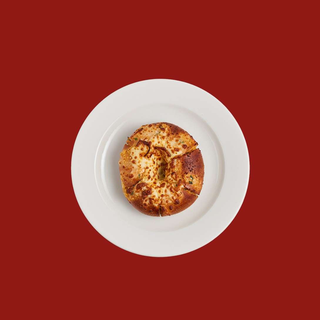 Cheese-topped bagel, sliced into four wedges, rests on a white plate, centered against a solid deep-red background.