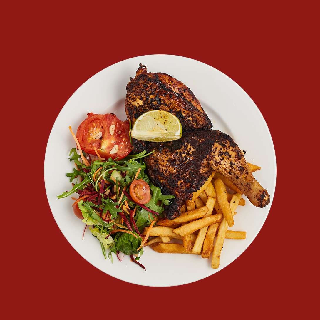 Half a cooked chicken served with salad, fries, cooked tomato, topped with a slice of lime.