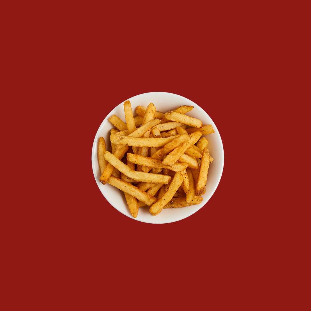Bowl of crispy seasoned French fries rests centered on a solid red background, emphasizing a simple, minimalistic snack presentation.