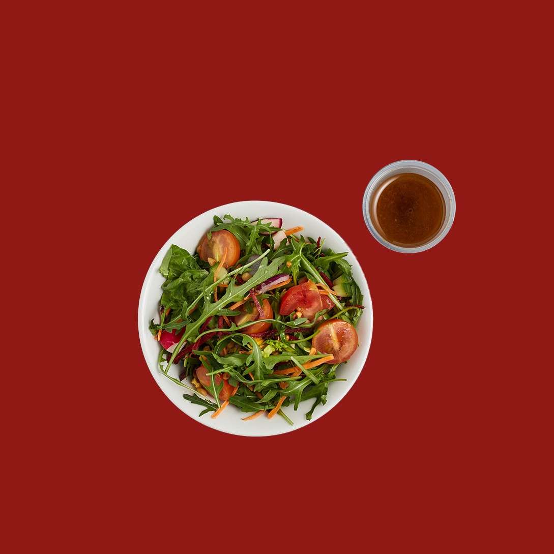 Mixed leaf salad with fresh vegetables and a pot of dressing.