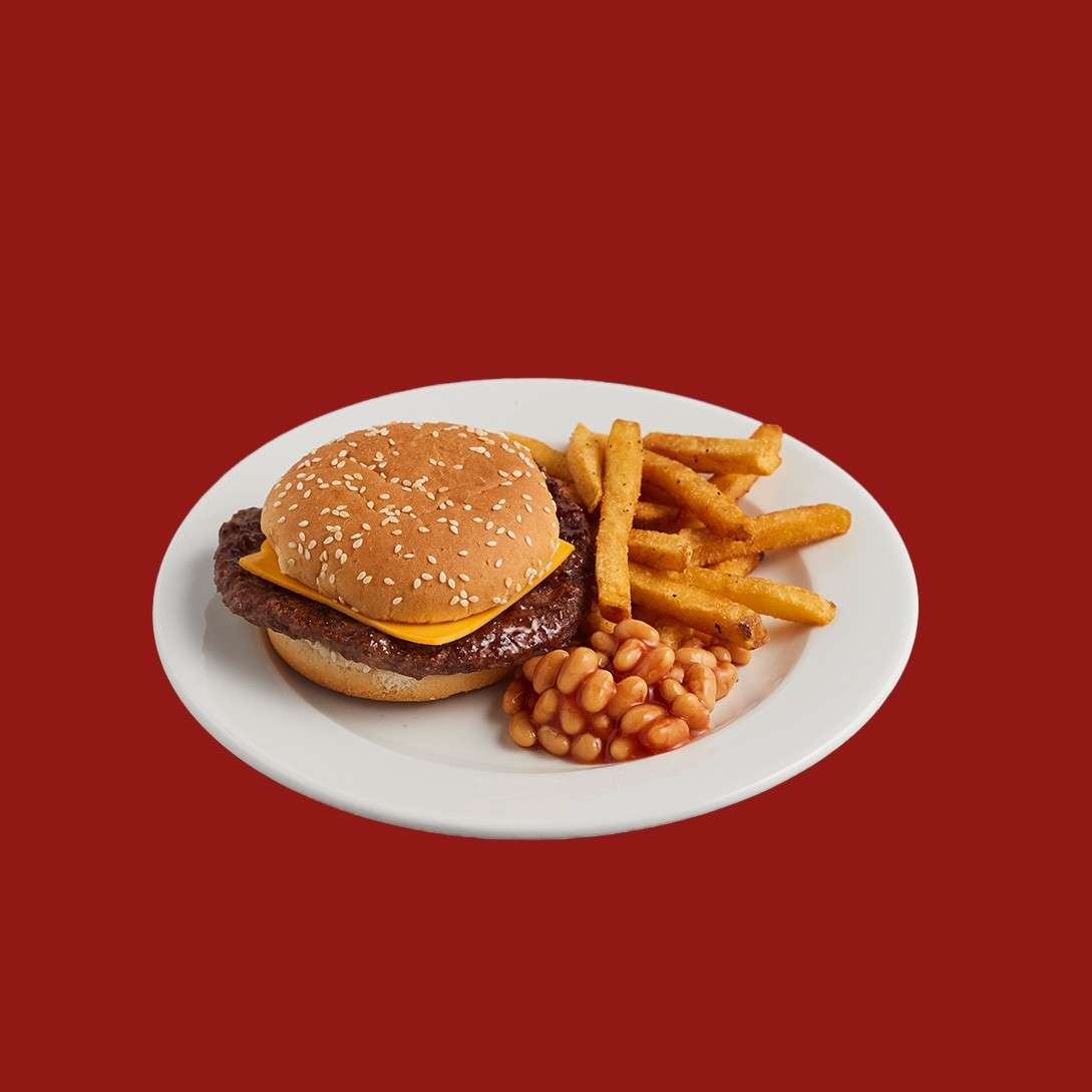 Cheeseburger rests on a white plate, accompanied by seasoned fries and a small serving of baked beans, set against a solid red background.