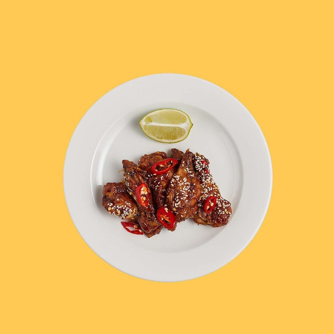 Hot wings in a Korean sauce topped with chilli and sesame seeds served with a slice of lime.