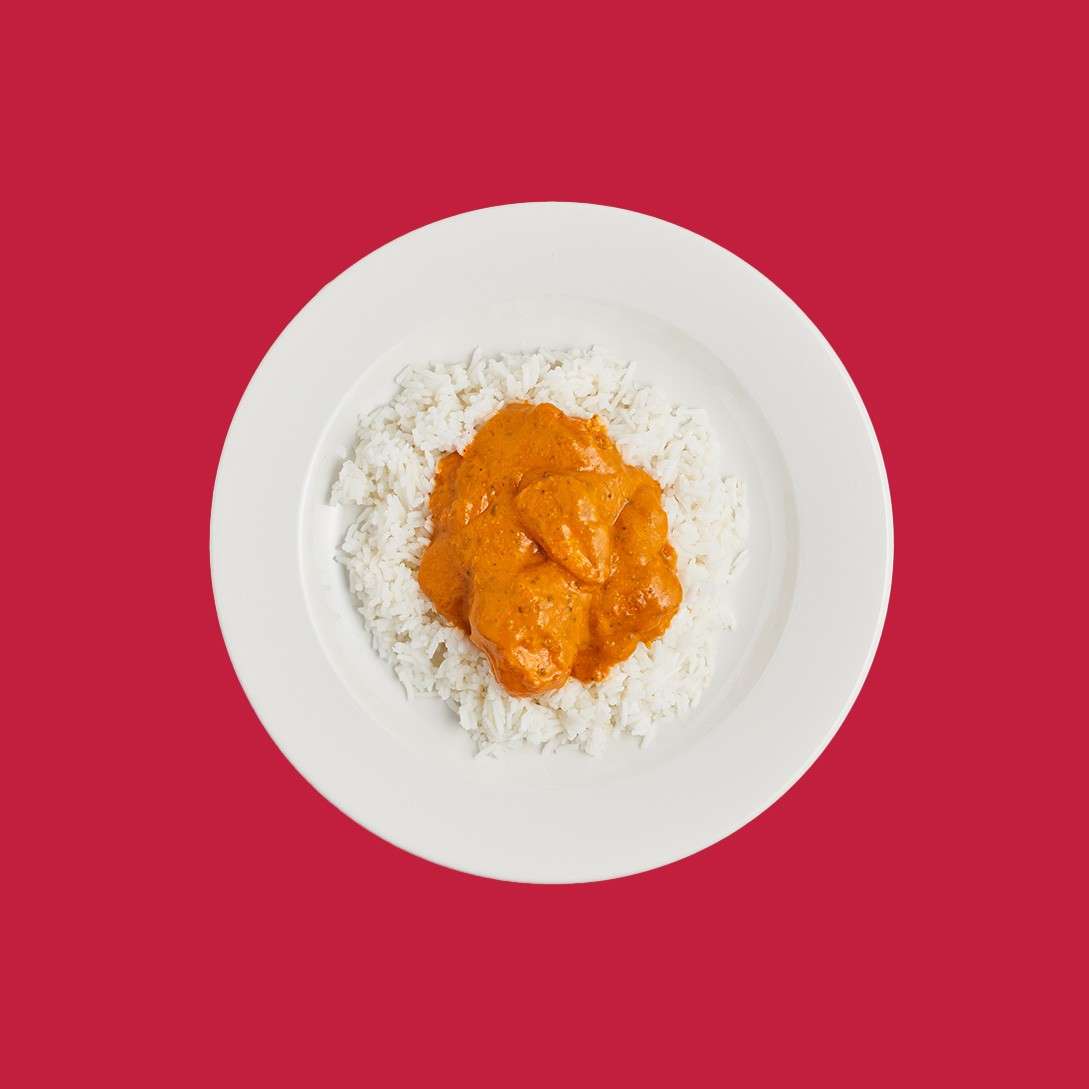 Rice with orange curry sits centered on a white plate, sauce-coated chunks resting on the rice, against a solid red background.