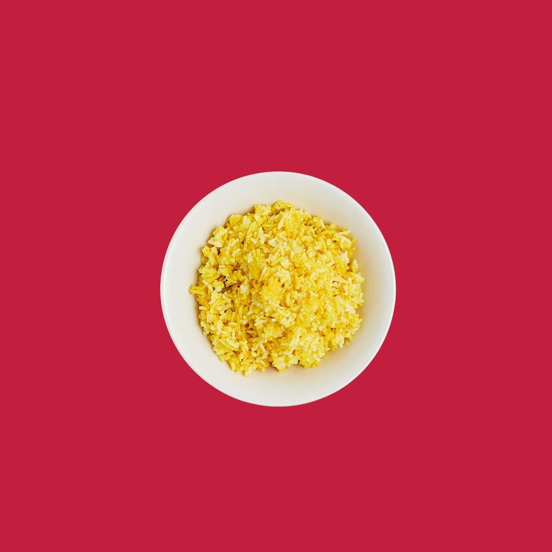 White bowl presents fluffy yellow fried rice, piled high, sitting centrally on a flat, solid red background with ample negative space surrounding the dish.