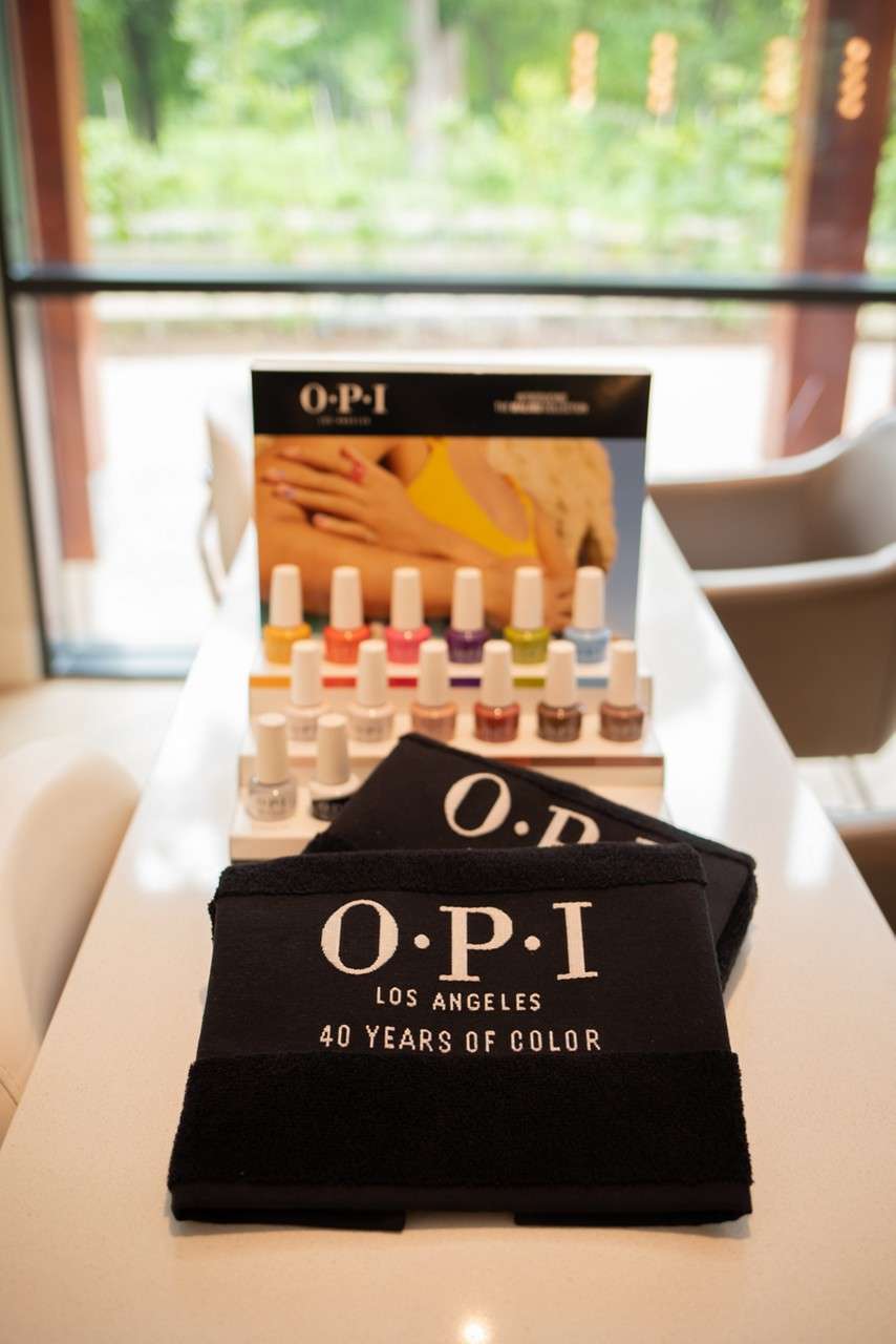 O·P·I Pro Spa products rest arranged; a tube and small bottle near green leaves, a wooden spoon, slate, and a bowl of dried herbs. Text: “O·P·I PRO SPA SKIN CARE HANDS & FEET MICRO-EXFOLIATING HAND POLISH,” “ULTRA-NOURISHING,” “O·P·I PRO SPA.”