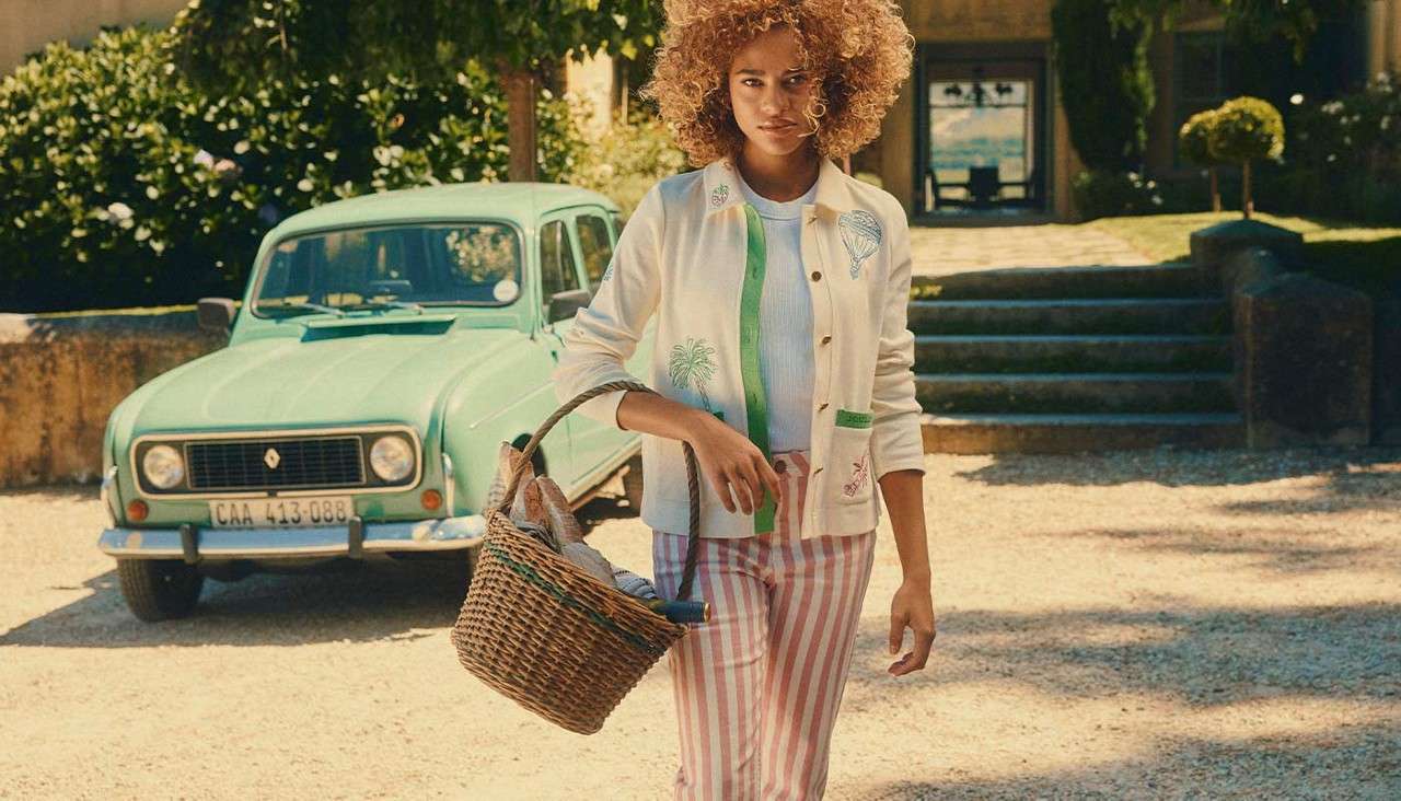 Woman carrying a basket wearing stripy trousers and a shirt with pops of colour.