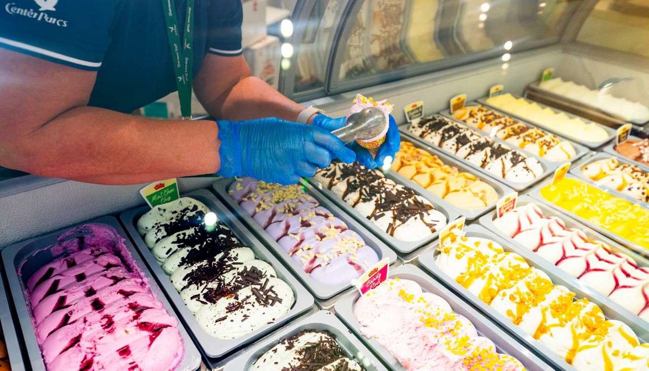 Staff me member scooping colourful ice cream. 