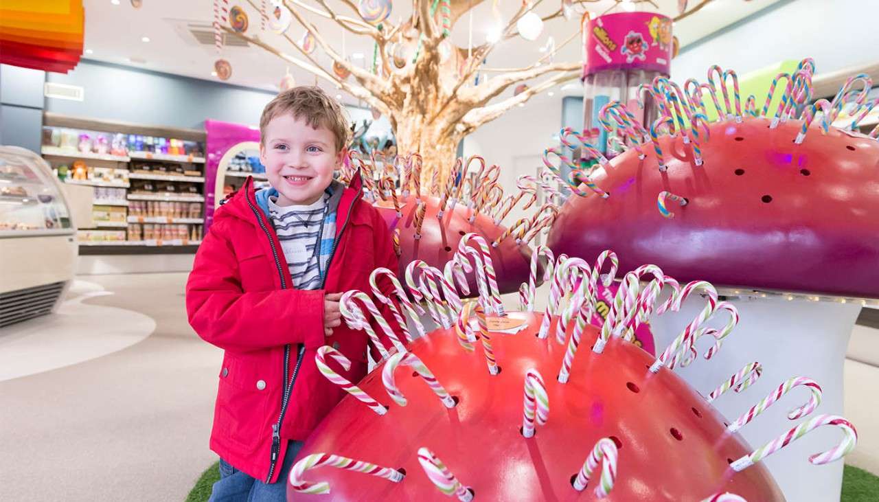 Child standing next to a toadstool with candy canes.