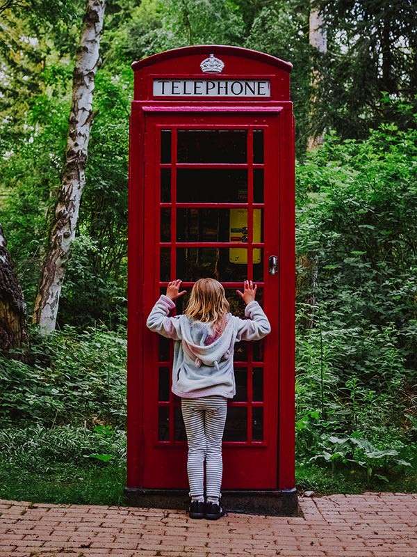 A child staring through the window of a red telephone box.