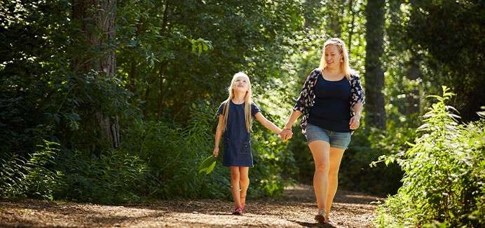 A mother and daughter walk through the sunny forest.