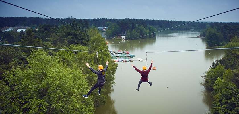Two people ziplining over the lake.